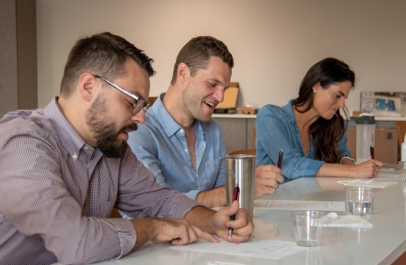 2 men and a woman sitting at a counter writing on paper