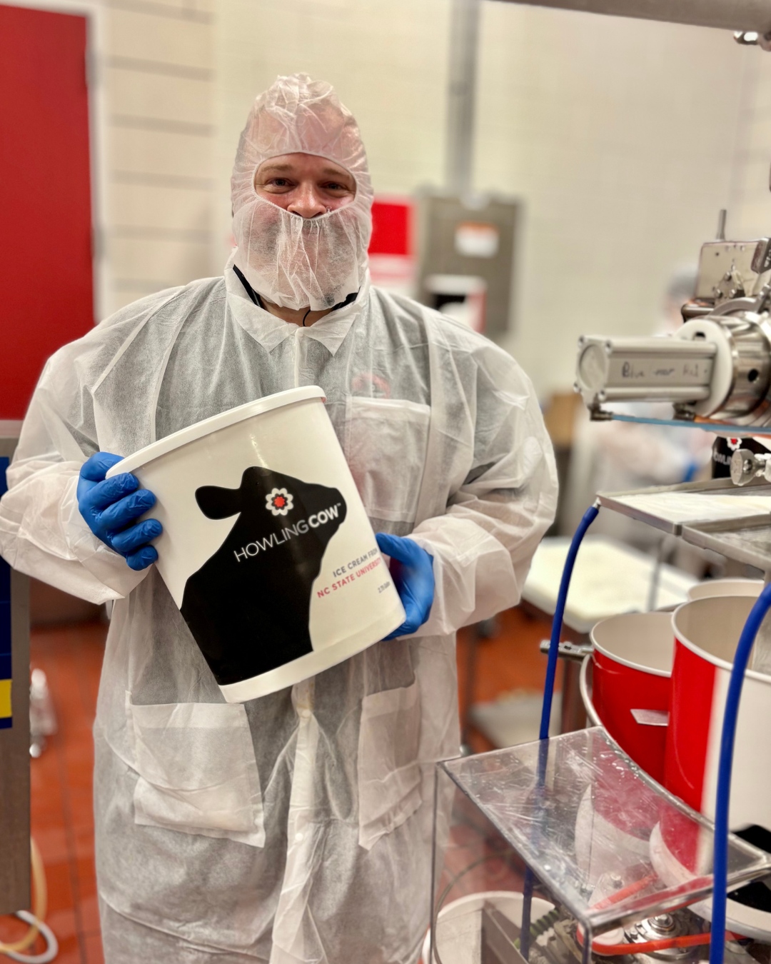 Man in mask and gown holding gallon of Howling Cow Ice Cream at NC State