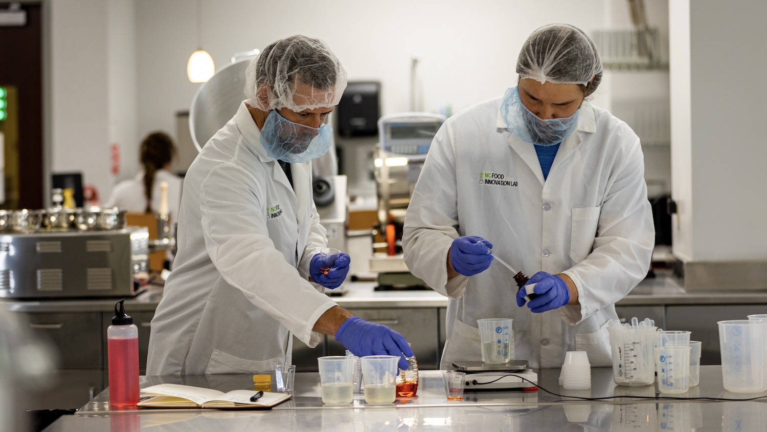 Two men in hair nets working in a food test kitchen at NC Food Innovation Lab