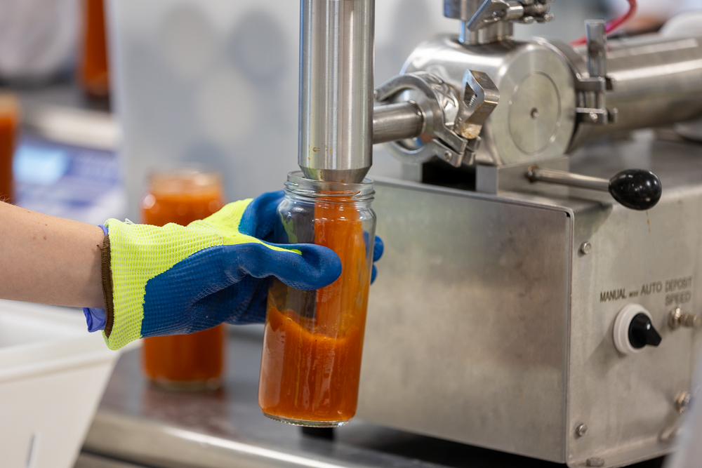 NCFIL member holding a glass jar under a machine that dispenses soup.